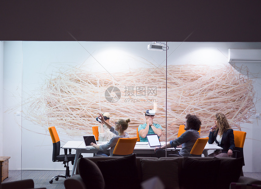 ‘~启动业务队夜间办公会议上用虚拟现实耳机,开发人员创意办公室的桌子周围与虚拟现实模拟器会  ~’ 的图片