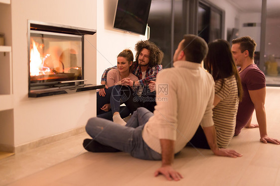 寒冷的冬夜,群轻的多民族夫妇坐壁炉前的地板上图片