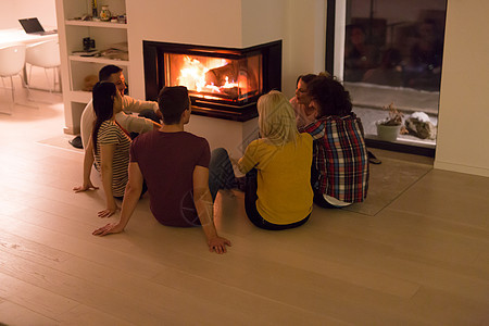 寒冷的冬夜,群轻的多民族夫妇坐壁炉前的地板上图片