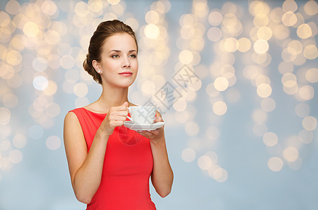 人,假日饮料的微笑的女人穿着红色的衣服,灯光的背景下喝杯咖啡图片