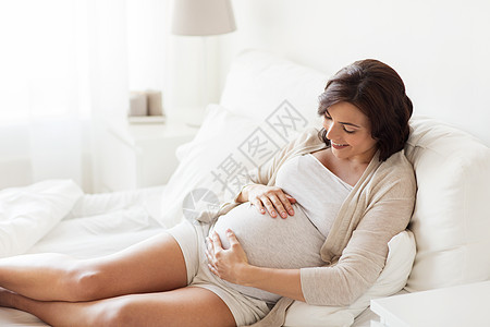 孕妇小孩怀孕,休息,人期望的快乐的孕妇躺床上,触摸她的肚子家里背景