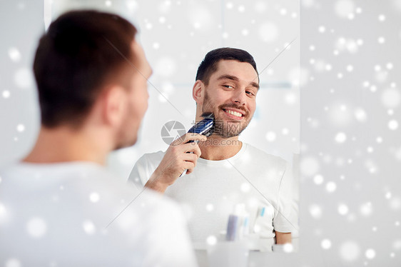 美容,剃须,美容人的轻人看着镜子剃须胡须与修剪机电动剃须刀家里浴室雪图片