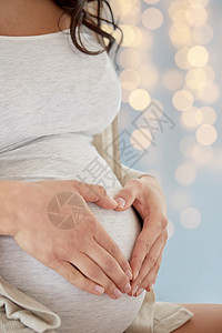 怀孕,爱,人期望的特写孕妇节日灯光背景下心脏手势图片