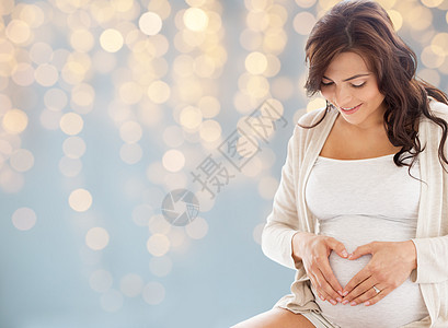 怀孕,爱,人期望的快乐的孕妇节日灯光背景上心脏手势图片