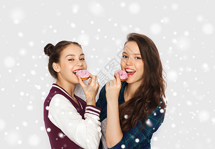 冬天,诞节,人,假日快餐的快乐的微笑,漂亮的十几岁的女孩朋友吃甜甜圈,并灰色背景雪上玩图片
