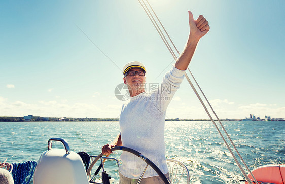 航海,龄,旅游,旅游人的快乐的老人戴着船长帽方向盘上,竖大拇指,帆船游艇漂浮海上图片