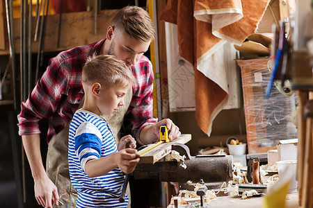 家庭,木工,木工人的父亲小儿子用尺子铅笔测量车间的木板图片