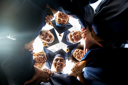 教育毕业结人的群快乐的国际学生穿着灰浆板学士服站圆圈里牵手图片