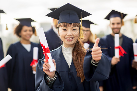 教育毕业手势人的群快乐的国际学生穿着灰浆板学士服,毕业证书竖大拇指图片