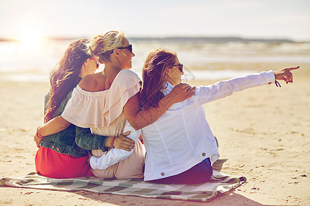 聚会轰趴暑假,假期,旅行人们的群微笑的轻女戴着太阳镜,坐沙滩毯子上,指着什么东西背景