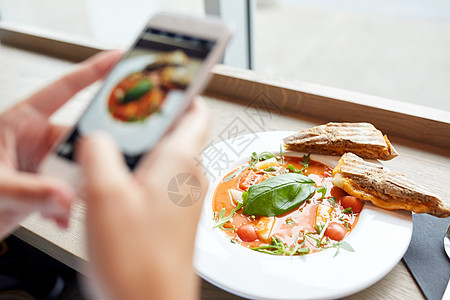 食物,饮食,技术,烹饪人的女人的手与Gazpacho汤照片智能手机屏幕上的餐厅图片