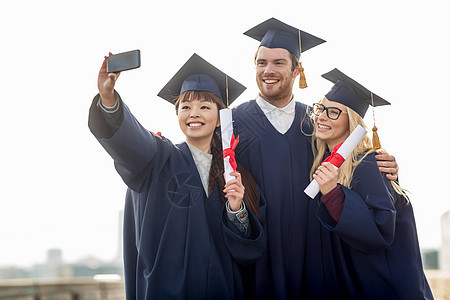 教育,毕业,技术人的群快乐的国际学生砂浆板学士学位礼服与文凭采取自拍智能手机户外图片