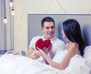 酒店,旅行,关系,假期幸福的微笑的夫妇床上与红色心形枕头背景图片