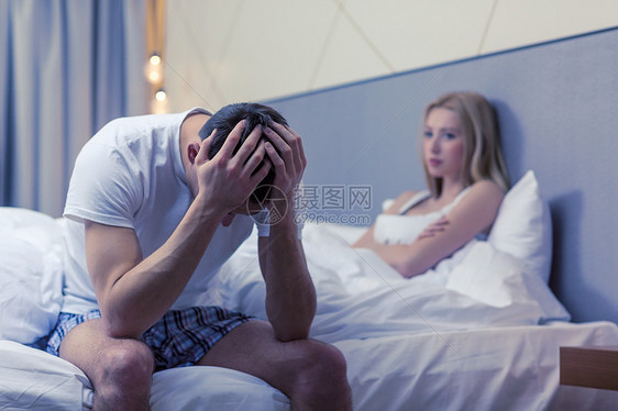 酒店,旅行,人际关系问题的心烦意乱的男人坐床上,女人坐后图片
