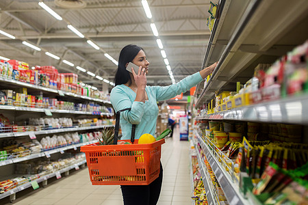 销售,购物,消费主义,沟通人的女人带着食物篮杂货店超市打电话给智能手机图片