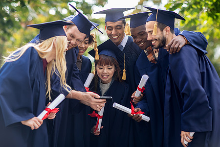 教育毕业人的群快乐的国际学生穿着灰浆板学士服,文凭智能手机图片