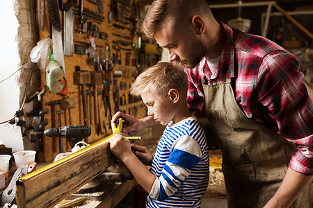 家庭,木工,木工人的父亲小儿子用尺子铅笔测量车间的木板图片