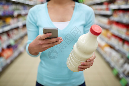 销售,购物,消费主义人的轻的妇女与智能手机持奶瓶杂货店超市图片
