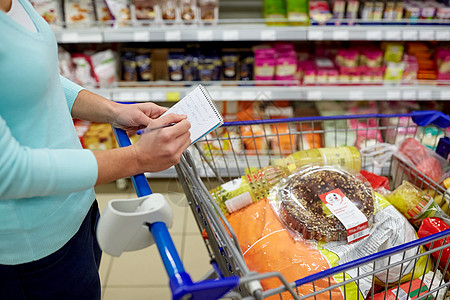 消费主义人的女人带着笔记本购物车手推车杂货店超市购买食物超市购物车里食物的女人图片