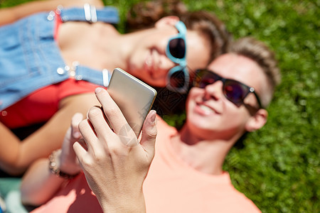 爱人的快乐的青少夫妇戴着太阳镜,智能手机躺草地上夏天快乐的十几岁的情侣智能手机躺草地上图片