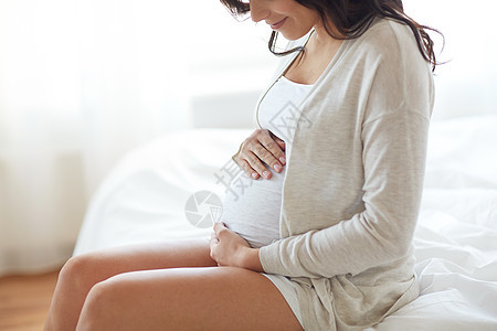 怀孕,休息,人期望的快乐微笑的孕妇坐床上,触摸她的肚子家里图片