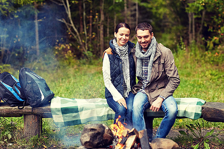 野营,旅行,旅游,徒步旅行人们的幸福的夫妇坐长凳上,树林的营火附近变暖图片