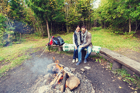 野营,旅行,旅游,徒步旅行人们的幸福的夫妇坐长凳上,拥抱附近的篝火树林里图片