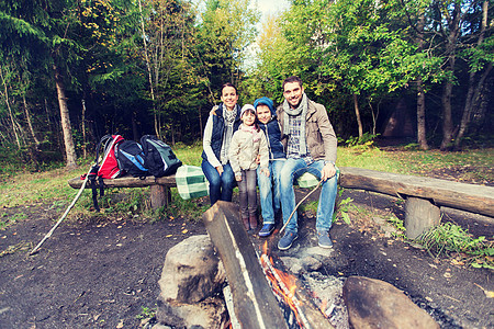 野营,旅游,徒步旅行人们的快乐的家庭坐长凳上的营地火灾树林里幸福的家庭坐篝火旁的长凳上图片