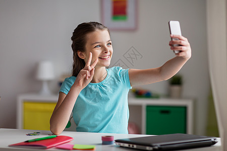 人,孩子技术女孩笔记本电脑智能手机自拍家里视频通话快乐的女孩带着智能手机家里自拍图片