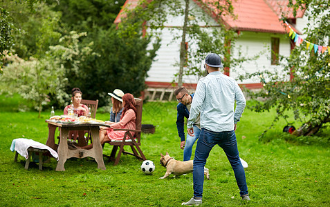 休闲,假期,人宠物的快乐的朋友夏天的花园聚会上狗踢足球朋友们夏天的花园里狗踢足球图片