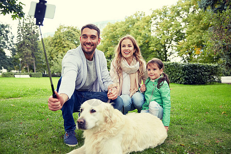 家庭,宠物,动物,技术人的快乐的家庭与拉布拉多猎犬狗公园的自拍杆上用智能手机拍照快乐的家庭与狗自拍智能手机图片