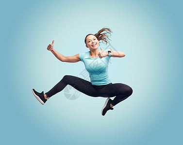 运动,健身,运动人们的快乐的微笑轻女人空中跳跃,并蓝色背景上竖大拇指快乐微笑运动的轻女人空中跳跃图片