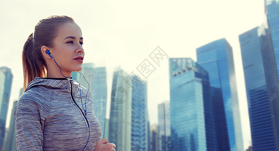 健身,运动,人,技术生活方式的快乐的女人跑步听音乐耳机新加坡城市摩天大楼的背景快乐的女人带着耳机城市里奔跑图片