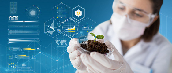科学生物学生态学研究蓝色背景虚拟图表上,用植物土壤样本手持培养皿,戴着保护具的轻女科学家科学家与植物图片