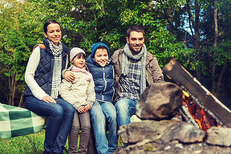 野营,旅行,旅游,徒步旅行人们的快乐的家庭坐长凳上,附近的营地交谈幸福的家庭坐篝火旁的长凳上图片