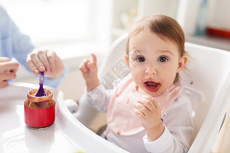 家庭,食物,饮食人的母亲与纯净物勺子喂养小婴儿坐高椅子家里母亲家用泥喂婴儿图片