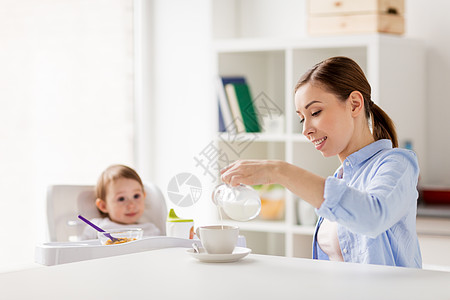 家庭,食物,饮食,早餐人们的快乐的母亲把牛奶水壶倒咖啡杯,小婴儿坐家里厨房的高椅子上快乐的母亲婴儿家里吃早图片