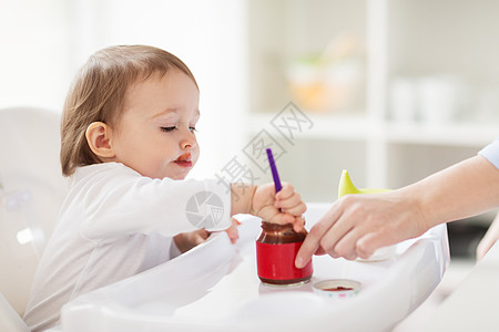 食物,孩子,喂养人的婴儿与勺子坐高椅子上,吃纯净的罐子家里婴儿用勺子家里吃罐子里的泥图片