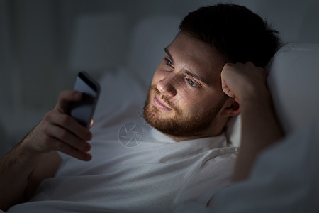 技术互联网通信人的轻人晚上家里的床上用智能手机发短信晚上床上智能手机的轻人图片