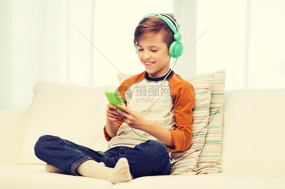 休闲,儿童,技术人的微笑男孩与智能手机耳机听音乐家里玩游戏家里智能手机耳机的快乐男孩图片