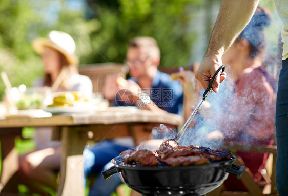 休闲,食物,人假日的男子烹饪肉烧烤为他的朋友夏季户外聚会夏天的聚会上,男人烧烤架上煮肉图片