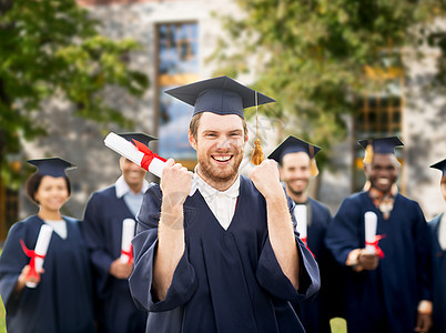 教育手势人的群快乐的国际学生穿着灰浆板学士学位礼服,校园建筑背景下庆祝成功毕业带着文凭庆祝毕业的快乐学生图片