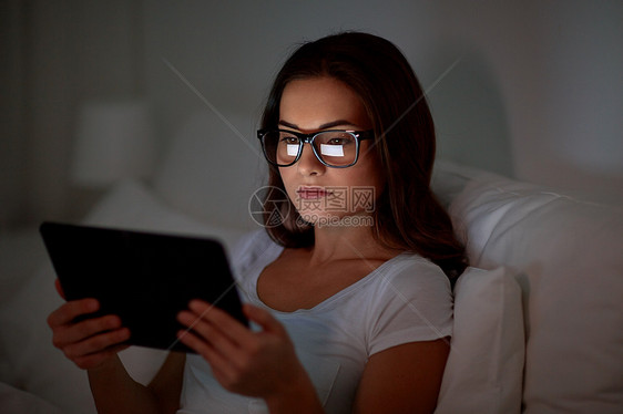 技术,视觉,交流人的轻的女人戴着眼镜,晚上家里的卧室床上用平板电脑家里床上戴眼镜平板电脑的女人图片