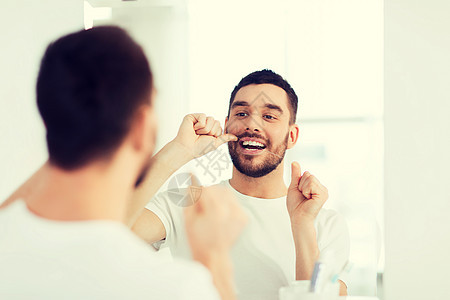 保健,牙科卫生,人美容微笑的轻人用牙线清洁牙齿,并家里的浴室照镜子浴室用牙线清洁牙齿的男人图片