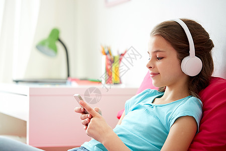孩子,技术人的快乐的女孩与智能手机耳机听音乐床上家家里智能手机耳机的快乐女孩图片