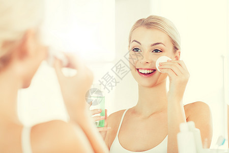 美丽,皮肤护理人的微笑的轻妇女应用乳液棉花盘,以洗她的脸浴室轻的女人浴室洗洗脸图片