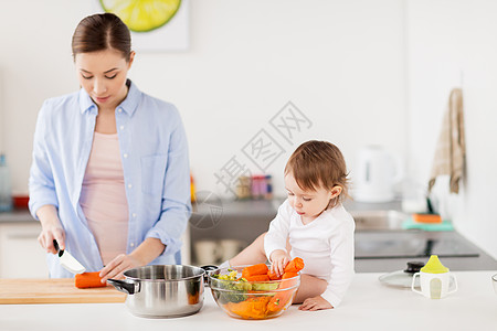 家庭,食物,健康饮食,烹饪人的快乐的母亲切胡萝卜小女婴与蔬菜锅家里厨房快乐的母亲婴儿家厨房饭图片