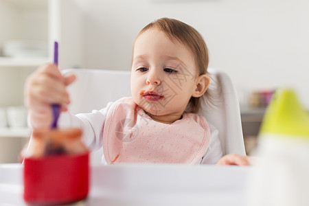 食物,孩子,喂养人的小女婴着勺子坐高椅子上,家里的厨房里吃罐子里的纯净物带勺子的女婴家吃罐子里的泥图片