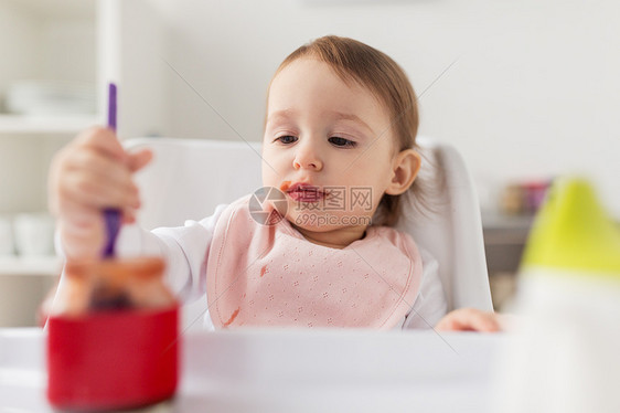 食物,孩子,喂养人的小女婴着勺子坐高椅子上,家里的厨房里吃罐子里的纯净物带勺子的女婴家吃罐子里的泥图片