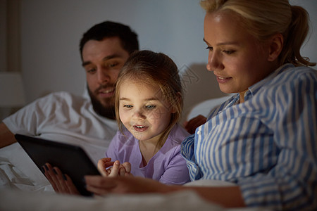 人,家庭技术的快乐的母亲,父亲小女孩床上的平板电脑电脑晚上家家里平板电脑的幸福家庭图片